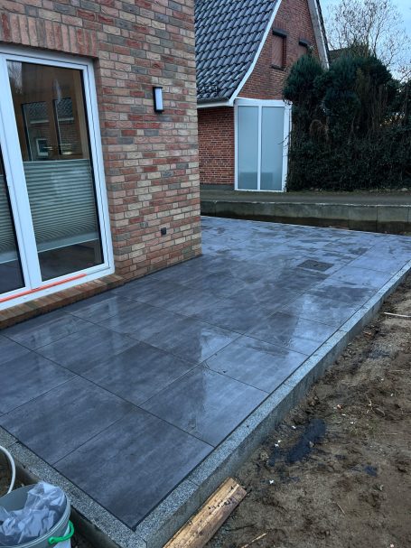 Gepflasterte Terrasse vor einem Haus mit neuem Bodenbelag und umgebendem Garten.